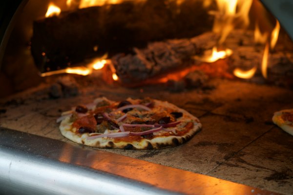 What safety measures are essential when installing a wood-fired pizza oven in a restaurant?